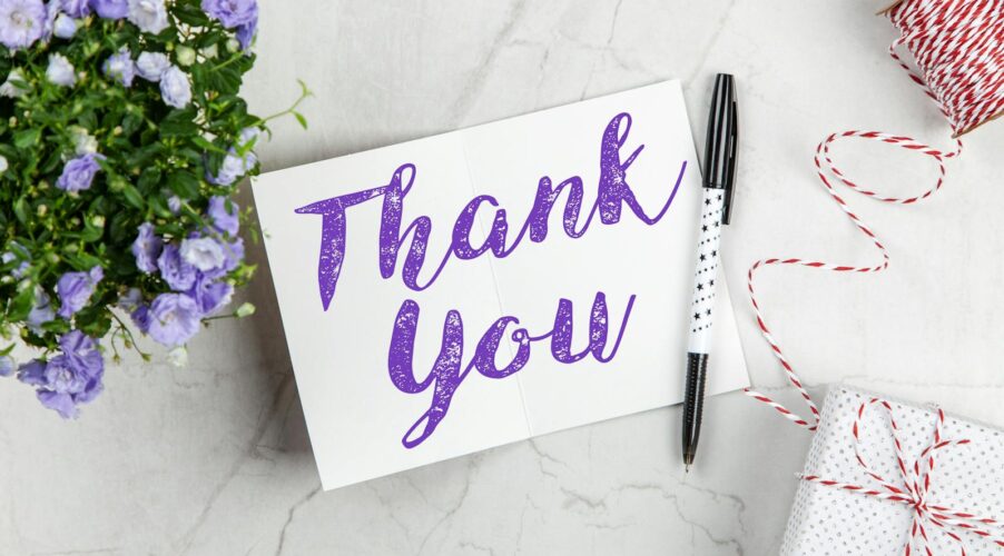 A stylish thank you card paired with purple flowers, a gift box, and pen on a marble surface.