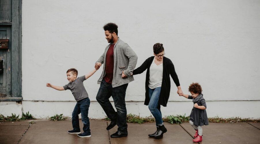 A joyful family walking together outdoors, holding hands in a playful and happy moment.