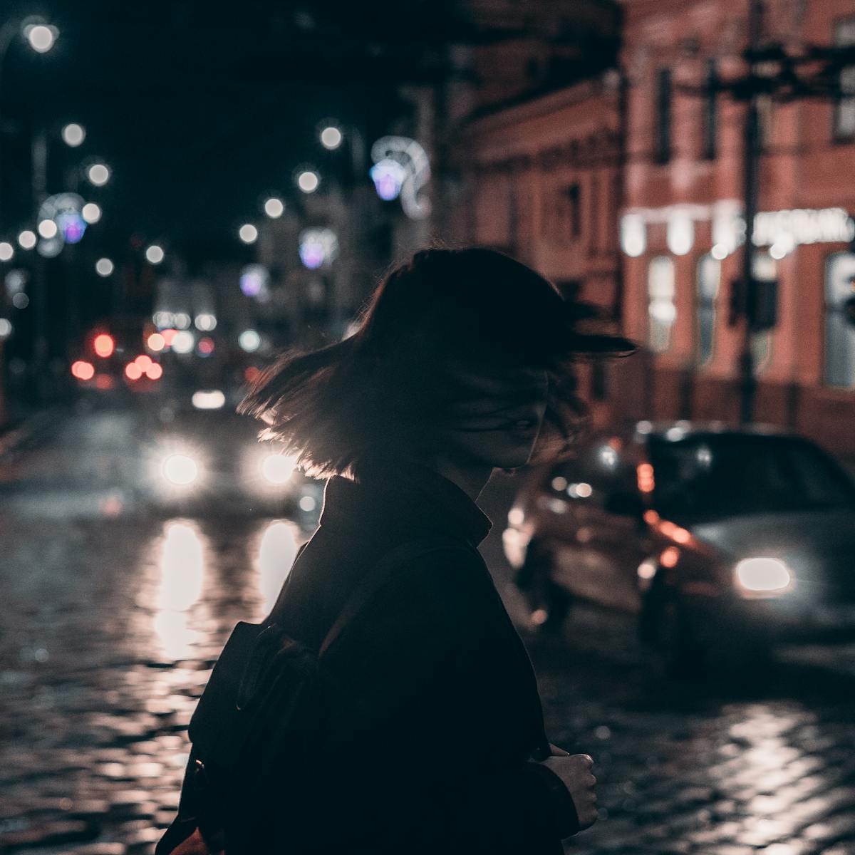 Silhouette of a woman walking on a bustling city street at night with blurred car lights.