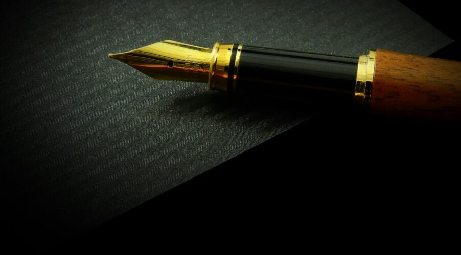 Detailed close-up of a classic fountain pen nib on textured black paper, showcasing elegance.