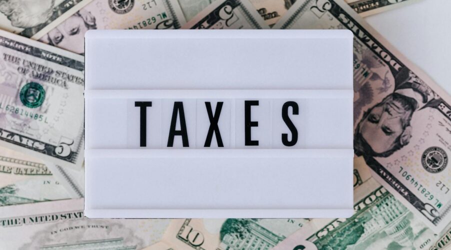 Top view of white vintage light box with TAXES inscription placed on stack of USA dollar bills on white surface